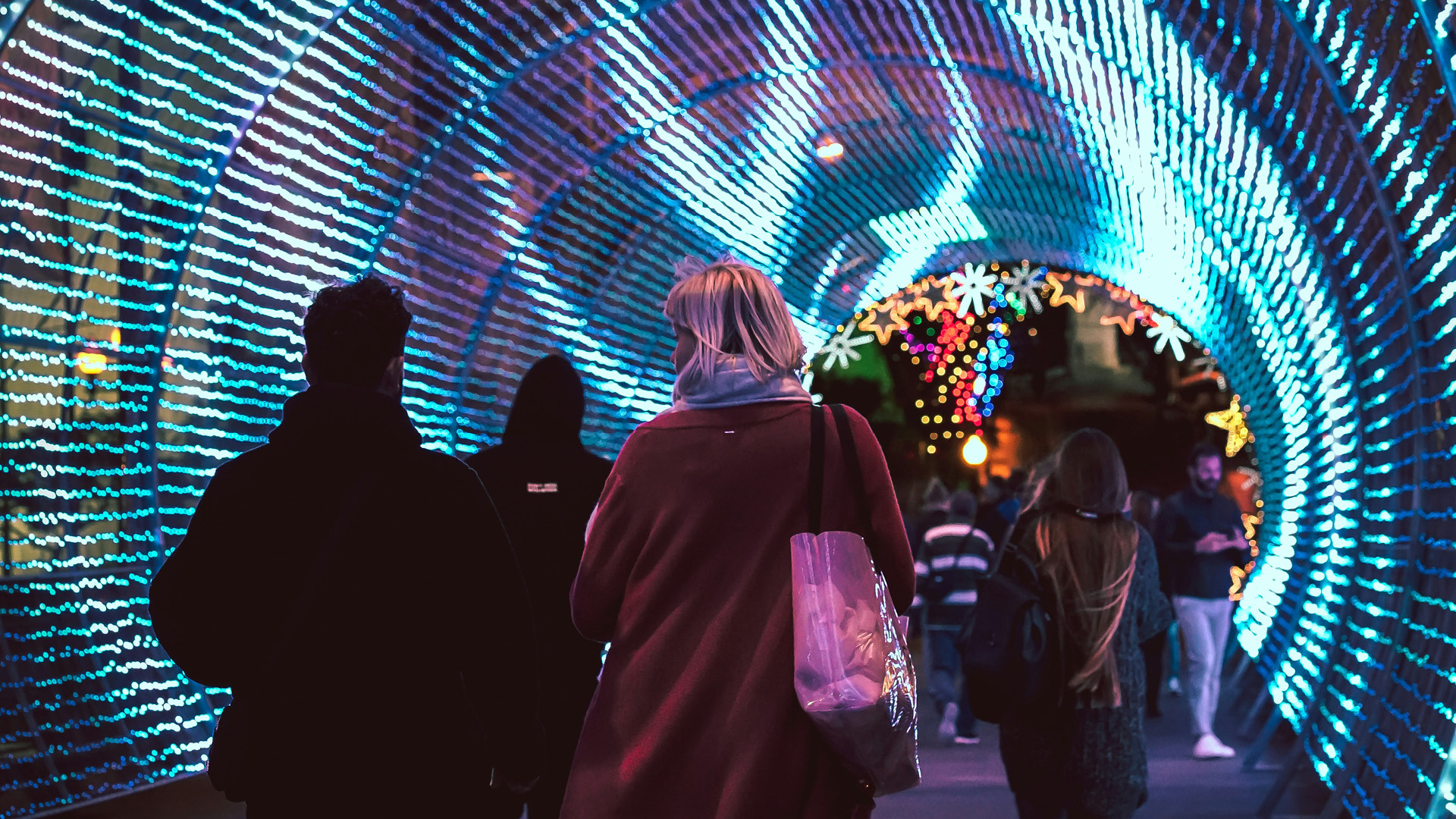 people walking through a christmas light tunnel